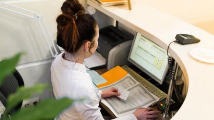 Eine Frau sitzt am Empfangstresen einer Arztpraxis und arbeitet am Computer