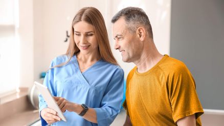 Eine gut gelaunte, junge Ärztin zeigt einem gut gelaunten Patienten medizinische Informationen auf ihrem Tablet