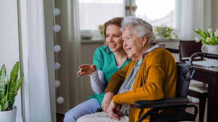 Krankenschwester und ihr älterer Kunde im Rollstuhl schauen aus dem Fenster