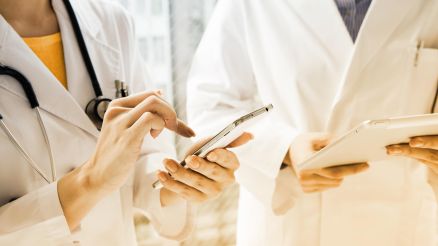 Eine Ärztin und ein Arzt mit weißen Kitteln halten Smartphones und Tablets in den Händen
