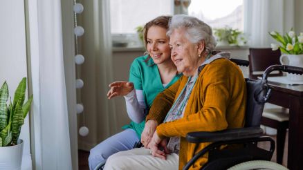 Krankenschwester und ihr älterer Kunde im Rollstuhl schauen aus dem Fenster
