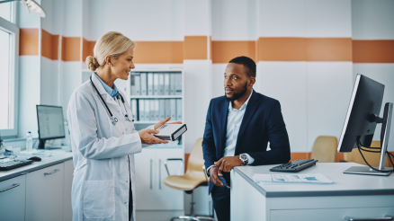 Eine Ärztin und ein TI-Techniker schauen sich an. Die Ärztin hält einen Konnektor in der Hand.
