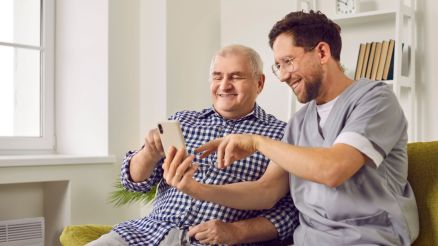 Ein junger Pfleger sitzt mit einem älteren Mann auf der Couch undvzeigt ihm die Funktionen von LifeTime Professional