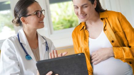 Hebamme zeigt schwangerer Frau medizinische Daten auf einem Tablet
