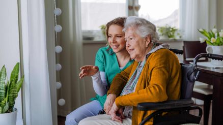 Krankenschwester und ihr älterer Kunde im Rollstuhl schauen aus dem Fenster