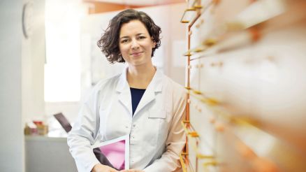 Apothekerin mit Tablet steht vor einem Regal mit Schubladen für Medikamente